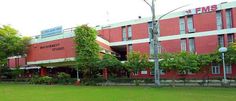 the building is red and white with many trees in front of it, along with green grass