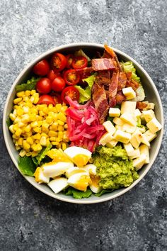 a bowl filled with different types of food on top of a gray table next to tomatoes and corn