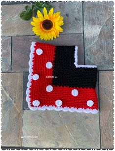 a crocheted mickey mouse blanket with a sunflower on the ground next to it