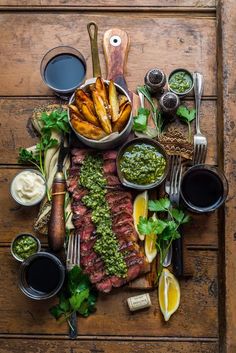 steak, french fries and sauces on a wooden table with utensils for dipping