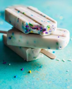 two popsicles with sprinkles on them sitting on a blue surface next to confetti