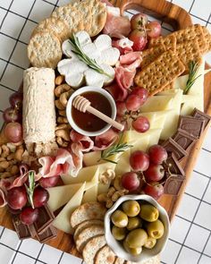 an assortment of cheeses, crackers and nuts on a wooden platter with grapes