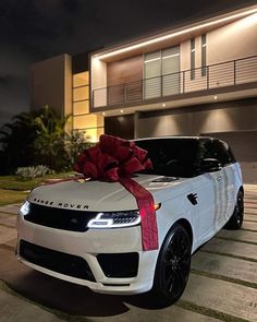 a white range rover with a red bow on it's hood parked in front of a house