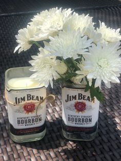 two jars filled with white flowers sitting on top of a wicker table next to a candle