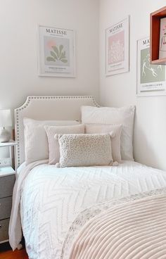 a white bed sitting in a bedroom next to two pictures on the wall above it