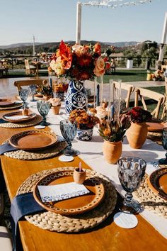 an outdoor table set with place settings and flowers in vases on the table top