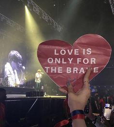 someone holding up a heart shaped sign with the words love is only for the brave on it