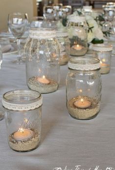 mason jars filled with sand and lit candles on top of a table covered in white flowers