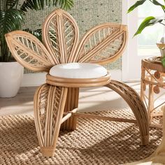 a wicker chair with a white cushion sits in front of a potted plant