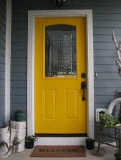 a yellow front door with welcome mat and potted plants on the side walk next to it