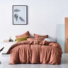 a bed with an orange comforter in a white room next to a cactus plant