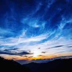 the sun is setting over mountains with clouds in the sky