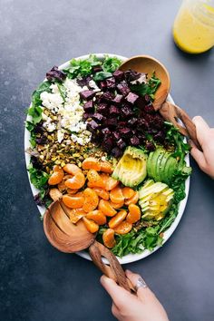 two hands holding wooden spoons over a plate of salad with avocado, lettuce and carrots