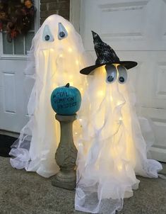 two halloween decorations with ghost faces and lights on the front door, one has a fake pumpkin in its mouth