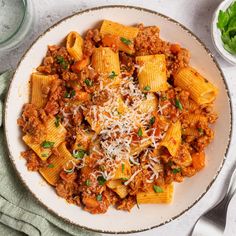 a white plate topped with pasta and meat covered in sauce next to parmesan cheese