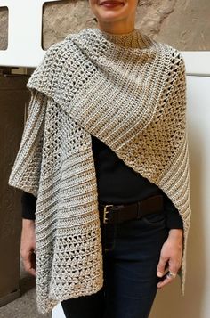 a woman standing next to a wall wearing a knitted shawl