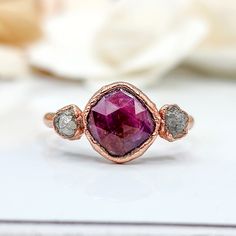 a close up of a ring with a pink stone and two white diamonds on it