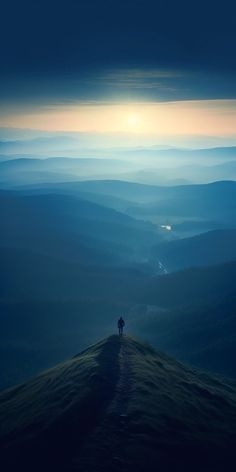 a person standing on top of a hill with the sun setting in the distance behind them