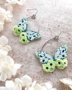 two green and blue butterfly shaped earrings on top of white flower petals in front of them