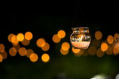 a glass jar hanging from a string with lights in the back ground and trees in the background