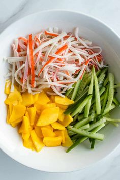 a white bowl filled with green beans, carrots and snap peas on top of a marble counter