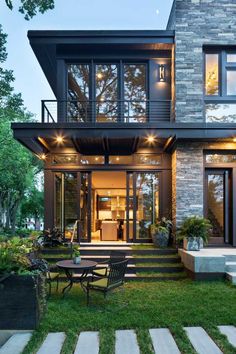 a modern house with stairs leading up to the front door and patio area, surrounded by grass