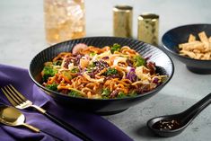 a bowl filled with noodles, broccoli and other foods next to some silverware