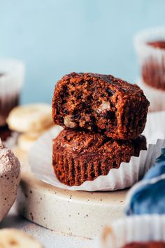 two chocolate muffins stacked on top of each other with bananas in the background