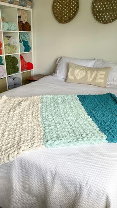 a bed with a blanket on top of it next to two wall shelves filled with blankets