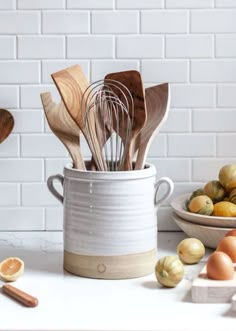 wooden utensils are in a white bucket with spoons and other kitchen items