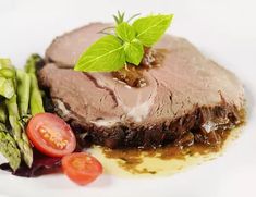 a piece of meat and asparagus on a white plate with sauce, garnished with a green leaf