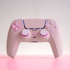 a pink video game controller sitting on top of a pink table next to a white wall