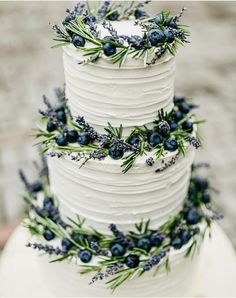 a three tiered white cake with blue berries and greenery