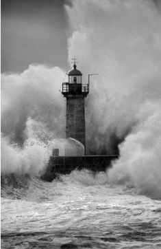 the lighthouse is surrounded by huge waves in black and white photo, with an ocean spray coming up behind it