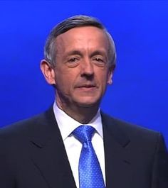 a close up of a person wearing a suit and tie with a microphone in front of him