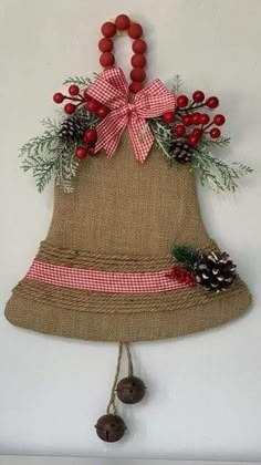 a burlocked bell hanging on the wall with pine cones and berries around it