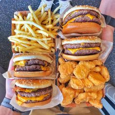 four hamburgers and fries are sitting on the table next to each other in trays