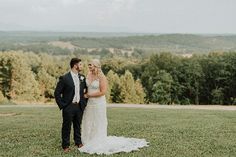 a bride and groom standing in the grass looking at each other with trees in the background