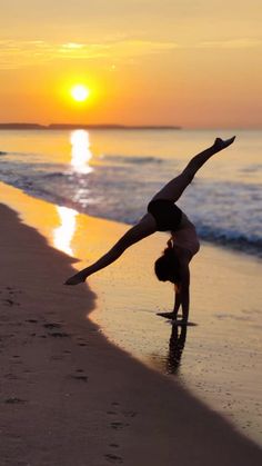 a woman doing a handstand on the beach at sunset