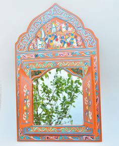 an orange and blue mirror sitting on top of a white wall next to a tree