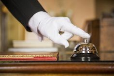 a hand in white gloves is on top of a desk with a book and a bell