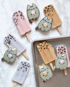 several popsicles with cats on them are sitting on a baking sheet and next to a cookie sheet