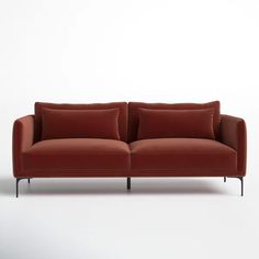 a red couch with two pillows on the back and one pillow on the side, in front of a white wall