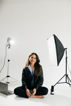 a woman sitting on the floor in front of a camera and lighting set up for a photo shoot