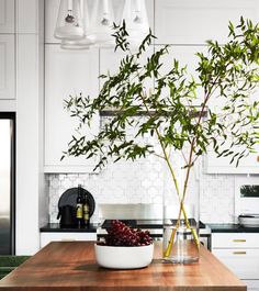 a vase with some plants in it sitting on a table next to a bowl of fruit