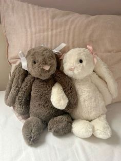 two stuffed animals sitting on top of a bed next to each other, one is gray and the other is white