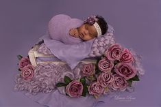 a baby sleeping on top of a purple blanket with pink roses around it and wearing a headband