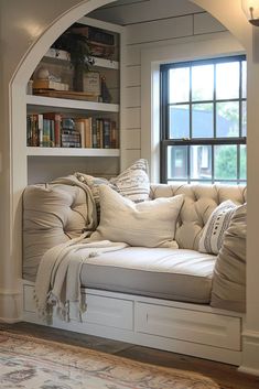 a window seat with pillows on it in front of a bookshelf