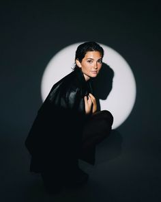 a woman sitting in front of a black and white circle with her shadow on the wall