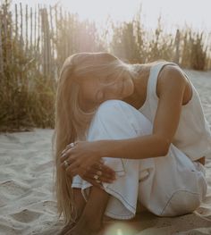 a woman sitting in the sand with her hands on her chest